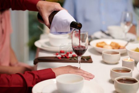 Photo for Man filling glass with red wine at family celebration - Royalty Free Image