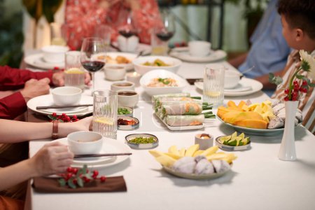 Téléchargez les photos : Famille vietnamienne manger à table avec des entrées et des plats traditionnels - en image libre de droit
