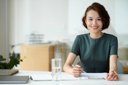 Photo for Portrait of female entrepreneur filling application form when working at office desk - Royalty Free Image