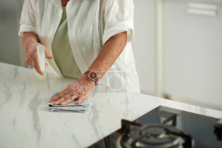 Téléchargez les photos : Mains de femme âgée essuyant comptoir avec détergent de nettoyage - en image libre de droit