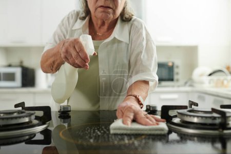 Photo for Senior woman cleaning dirty stove with detergent after cooking - Royalty Free Image