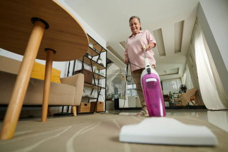 Foto de Alfombra de limpieza al vacío mujer senior en sala de estar - Imagen libre de derechos