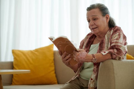 Téléchargez les photos : Femme âgée lisant un livre captivant à la maison - en image libre de droit