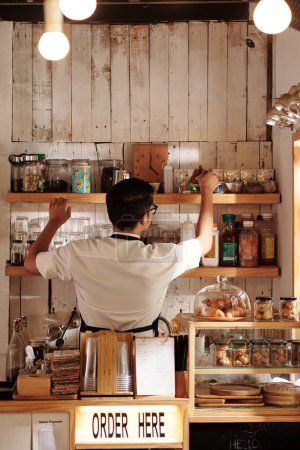 Foto de Café barista limpiando estantes y llenando tarros de té y café - Imagen libre de derechos