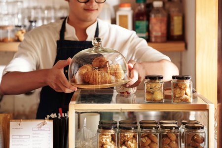 Téléchargez les photos : Image recadrée d'un serveur de café mettant une assiette avec des croissants frais sur le comptoir pour vendre - en image libre de droit