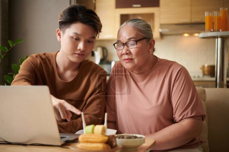 Téléchargez les photos : Jeune homme mettant routeur sans fil dans la maison dans sa grand-mère et expliquant comment cela fonctionne - en image libre de droit