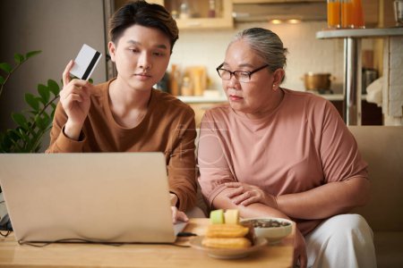 Photo for Young man helping grandmother to pay for online purchases with credit card - Royalty Free Image