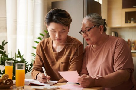 Photo for Young man explaining grandmother how to track expenses - Royalty Free Image
