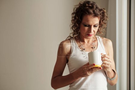 Photo for Pensive mature woman looking inside empty cup of coffee - Royalty Free Image