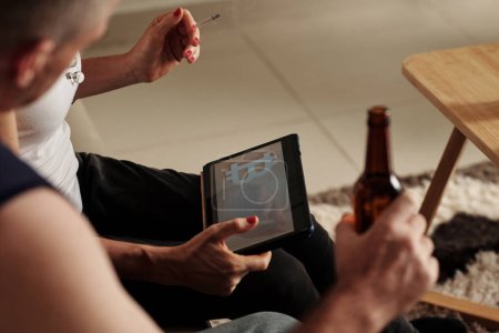 Téléchargez les photos : Couple mature fumant et buvant de la bière lors de la lecture de l'article sur Bitcoin prévision des prix - en image libre de droit