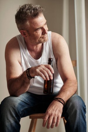 Téléchargez les photos : Pensive homme mûr avec chaume boire une bouteille de bière et détourner les yeux - en image libre de droit