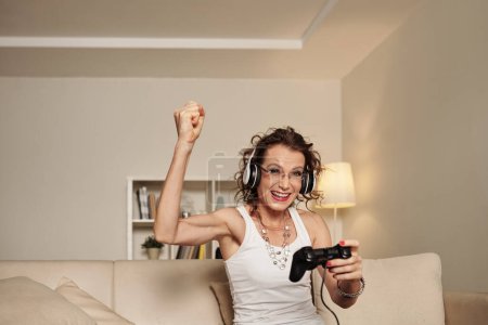 Foto de Retrato de feliz emocionado glam rock mujer madura celebrando ganar en videojuego - Imagen libre de derechos
