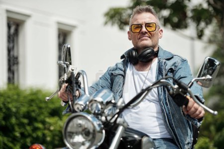 Téléchargez les photos : Élégant mature l'homme dans jaune lunettes de soleil équitation sur moto - en image libre de droit
