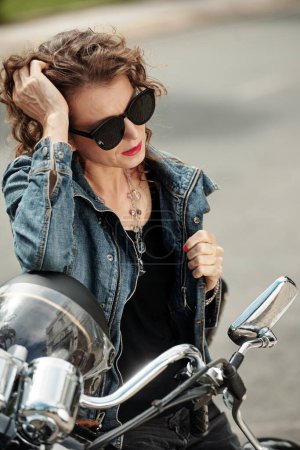 Téléchargez les photos : Portrait de élégant assis sur la moto, toucher ses cheveux et détourner les yeux - en image libre de droit