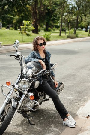 Photo for Stylish mature woman in susnglasses leaning on motorcycle when waiting boyfriend outside - Royalty Free Image