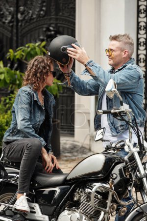 Photo for Smiling mature man helping girlfriend to wear motorcycle helmet - Royalty Free Image