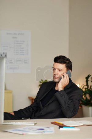 Photo for Portrait of serious businessman calling on phone to colleague after reading his report - Royalty Free Image