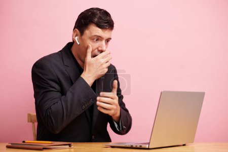 Téléchargez les photos : Incroyable homme d'affaires émotionnel couvrant mounth avec la main lors de la lecture de nouvelles choquantes sur ordinateur portable - en image libre de droit