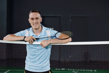 Téléchargez les photos : Joueur de badminton professionnel souriant debout au filet avec raquette à la main - en image libre de droit