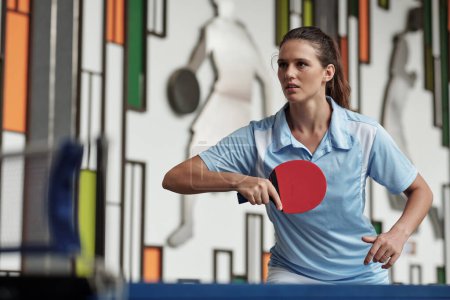 Foto de Decidida joven mujer jugando al tenis de mesa en el gimnasio - Imagen libre de derechos