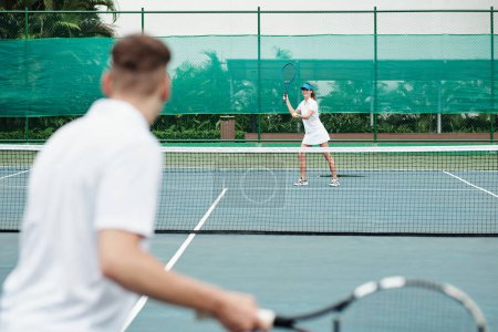 Téléchargez les photos : Sourire jeune femme servant ballon lorsque vous jouez au tennis avec un ami - en image libre de droit