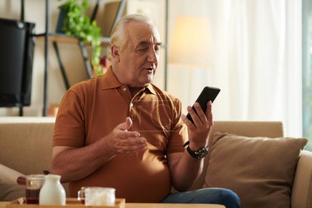 Foto de Hombre mayor positivo sentado en el sofá en casa y vídeo llamando a su mejor amigo o miembro de la familia - Imagen libre de derechos