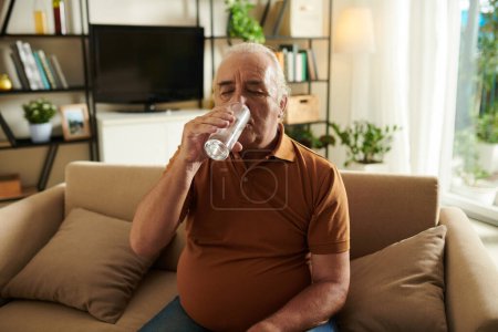 Téléchargez les photos : Homme âgé buvant un verre d'eau après avoir avalé le comprimé - en image libre de droit