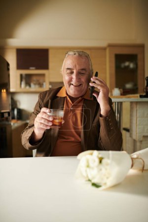 Téléchargez les photos : Heureux homme âgé excité boire un verre de whisky avant d'aller à ce jour poing temps dans un long temps - en image libre de droit