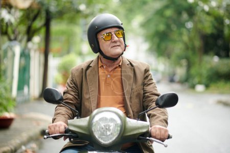 Téléchargez les photos : Homme âgé en lunettes de soleil et casque à travers la ville - en image libre de droit
