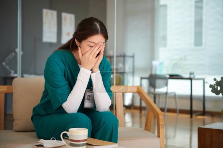 Foto de Enfermera médica sentada en el banco en la sala de estar y llorando después de perder al paciente - Imagen libre de derechos