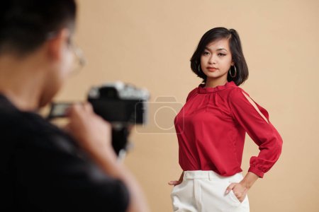 Téléchargez les photos : Jeune femme en chemisier de soie rouge foncé et pantalon blanc photographiant pour le magasin sur le marché commercial - en image libre de droit