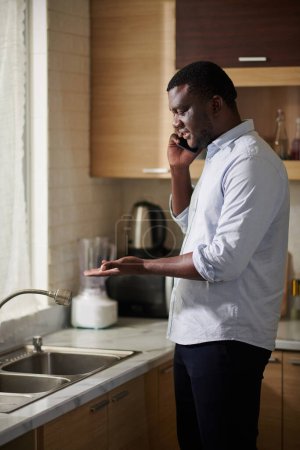 Téléchargez les photos : Homme noir appelant le propriétaire pour parler de fuite robinet de cuisine - en image libre de droit