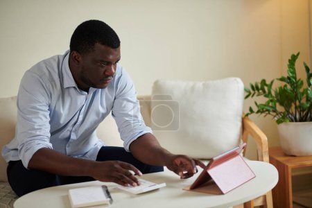 Téléchargez les photos : Homme utilisant planificateur de finances en ligne sur tablette informatique pour suivre les revenus et les dépenses - en image libre de droit