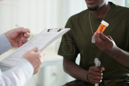 Photo for Ex-soldier holding container with pills prescribed by his doctor against severe migraine - Royalty Free Image
