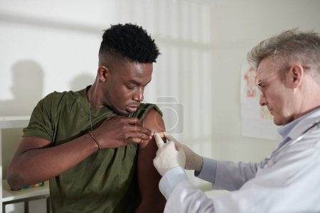 Foto de Médico pegando vendaje adhesivo en el lugar de inyección de la vacuna en el brazo del soldado - Imagen libre de derechos
