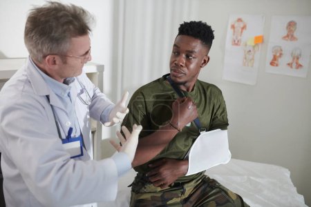 Téléchargez les photos : Docteur expliquant à l'homme militaire avec le bras cassé comment s'adapter à vivre avec la fronde - en image libre de droit