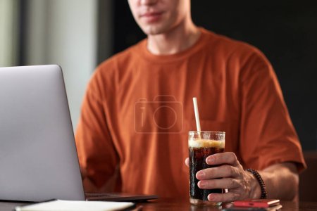 Téléchargez les photos : Jeune programmeur ayant boisson sucrée non alcoolisée lors du codage sur ordinateur portable - en image libre de droit