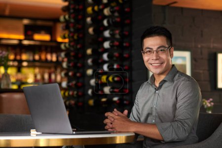 Photo for Portrait of smiling entrepreneur working on laptop at table in restaurant - Royalty Free Image