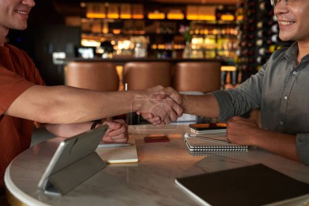 Téléchargez les photos : Image recadrée de partenaires commerciaux positifs serrant la main à la table du café avant de discuter du travail - en image libre de droit