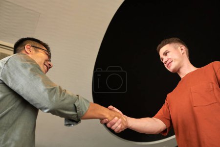 Photo for Cheerful young businessman greeting project founder, shaking his hand - Royalty Free Image