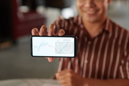 Photo for Smiling trader showing smartphone with chart on screen - Royalty Free Image