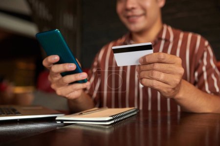 Photo for Cropped image of smiling man paying with credit card when shopping in mobile application - Royalty Free Image