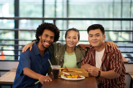 Photo for Portrait of hugging smiling friends sitting at table with box pizza and street food - Royalty Free Image