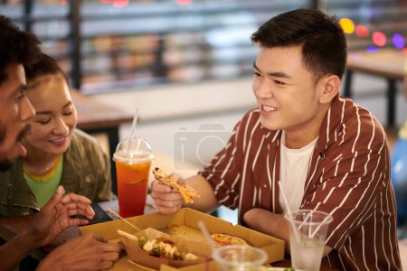 Photo for Cheerful Vietnamese young man spending time with friends eating pizza and talking - Royalty Free Image