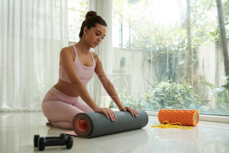 Photo for Young sportswoman rolling out yoga mat to exercise in the morning - Royalty Free Image