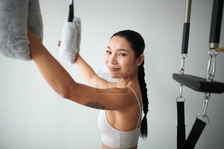 Foto de Retrato de la joven deportista asiática feliz haciendo varios ejercicios en la parte superior del cuerpo en una máquina especial - Imagen libre de derechos