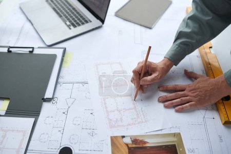 Photo for Hands of construction worker checking details of blueprint on his desk - Royalty Free Image