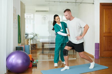 Photo for Nurse controlling man with injured knee doing lunges to strengthen muscles - Royalty Free Image