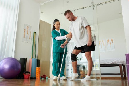 Foto de Enfermera apoyando a paciente aprendiendo a pisar pierna herida apoyándose en muleta - Imagen libre de derechos
