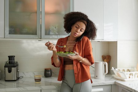 Foto de Ajuste mujer comer ensalada de verduras para el almuerzo y hablar por teléfono con un amigo o entrenador de fitness - Imagen libre de derechos